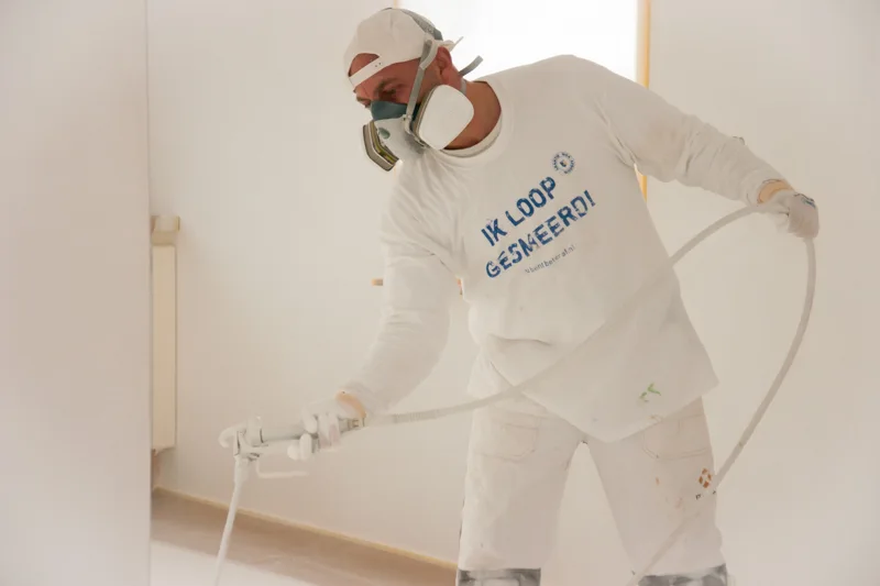 Schot Stukadoor aan het werk met airless spuitapparatuur en beschermende kleding