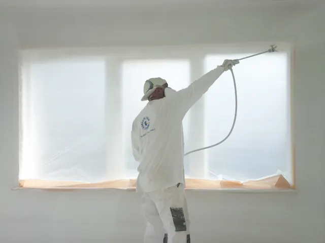 Vakman spuit een gladde muur naast een afgeplakt raam