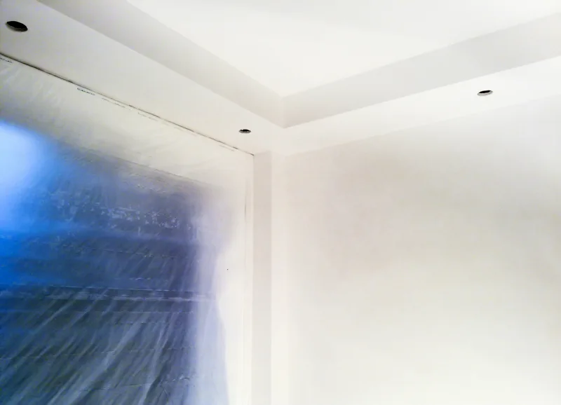 Schot Stukadoor brengt airless latex aan op het plafond van een zorgvuldig afgeplakte woning